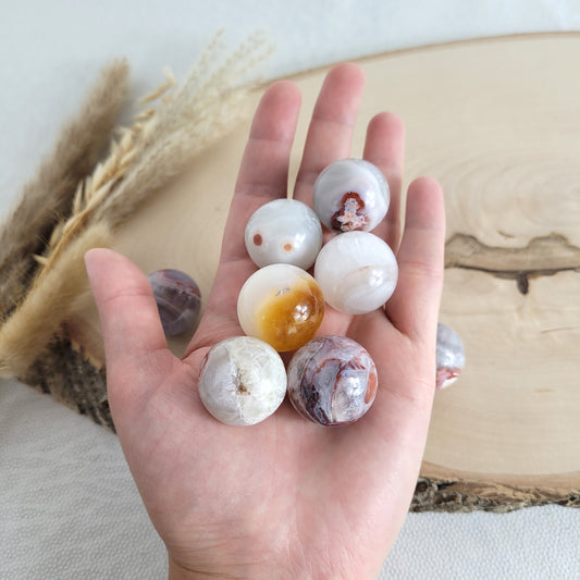 Chalcedon Kugel Mini geschliffen, liegend auf einer runden Holzscheibe mit sichtbarer Maserung – zeigt natürliche Farben, Muster und Kristallstrukturen.