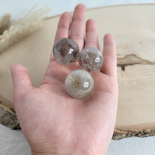 Rutilquarz Kugel mit feinen goldenen Rutil-Einschlüssen auf runder Holzscheibe präsentiert – natürliche Kristallstruktur mit faszinierendem Glanz.